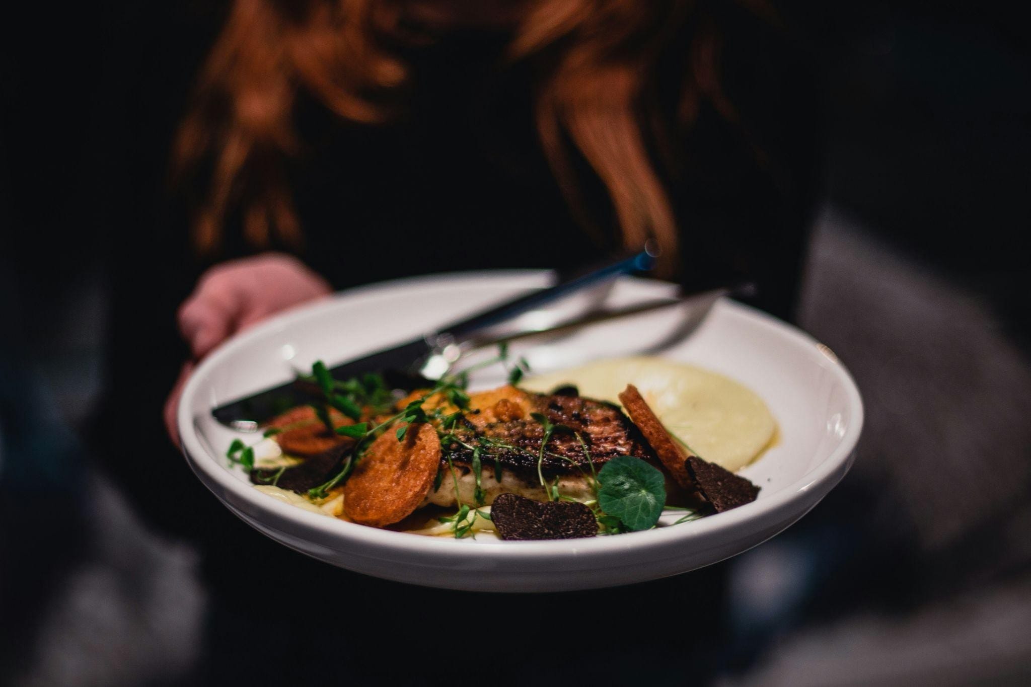 Hand offering a plate of decadent food in a shallow white bowl to the camera